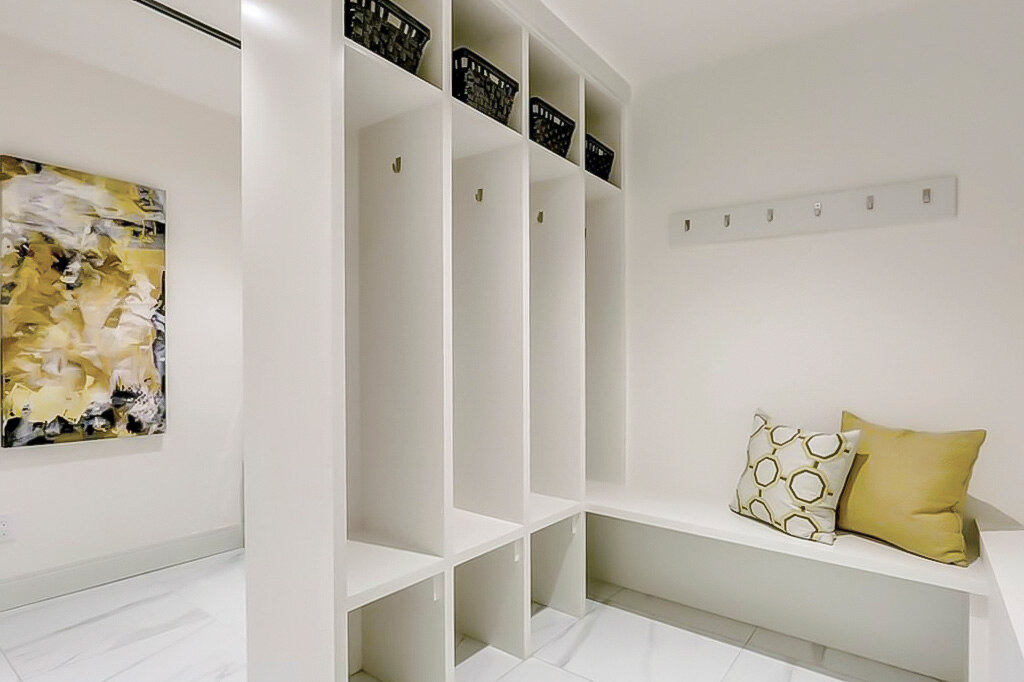 White built-in mudroom cabinets with vertical cubbies, hooks, and bench seating, designed to create a seamless built-in storage look for coats, bags, and shoes.