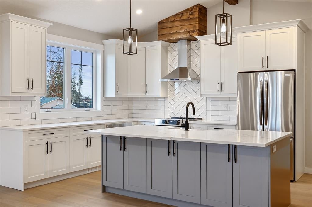 Kitchen showcasing choosing the right finish for your space with white cabinetry, contrasting grey island, stainless steel appliances, and modern lighting