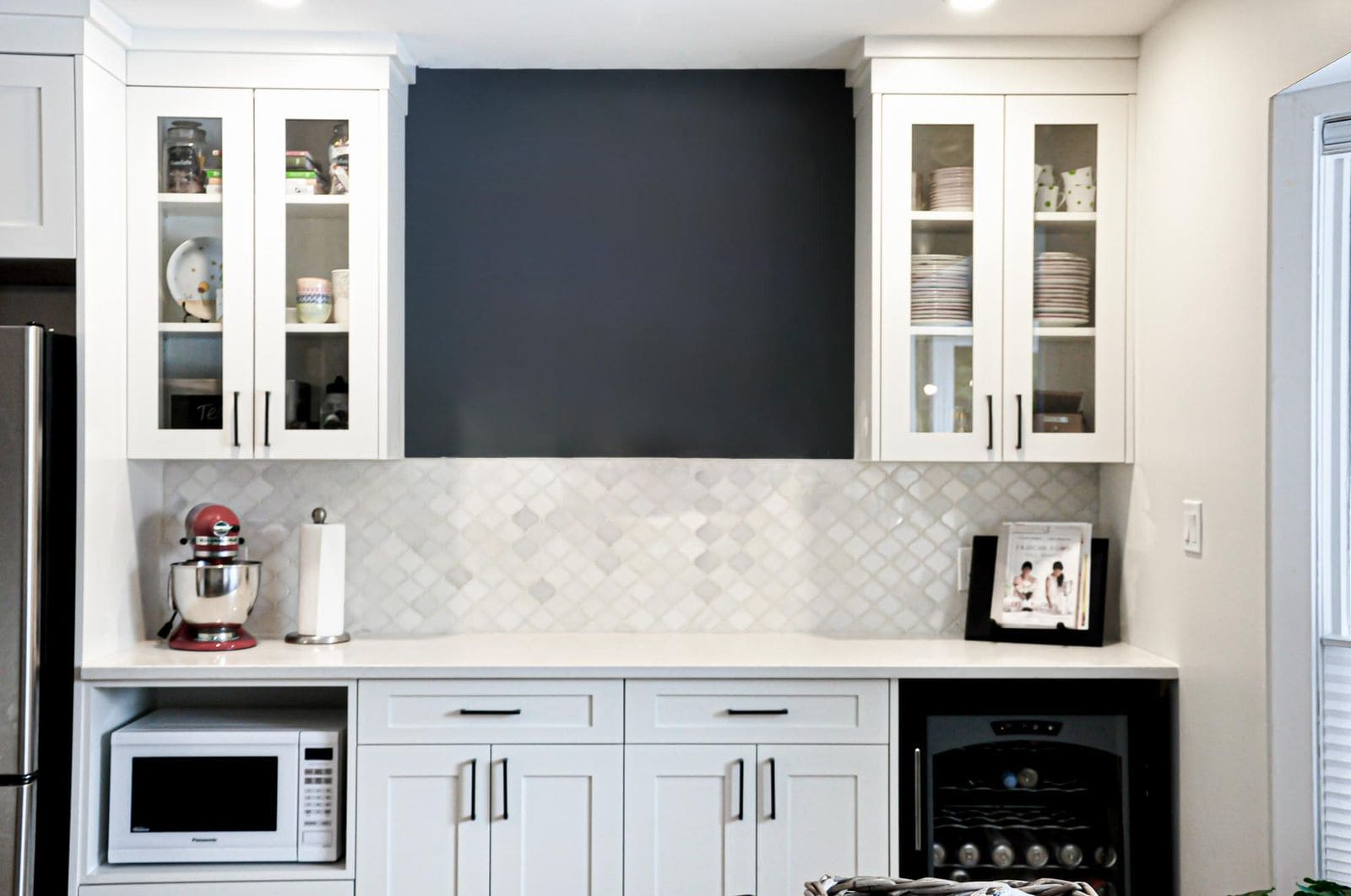 Wet bar showcasing elevated materials and finishes with white cabinetry, glass-front uppers, tile backsplash, and built-in wine fridge.