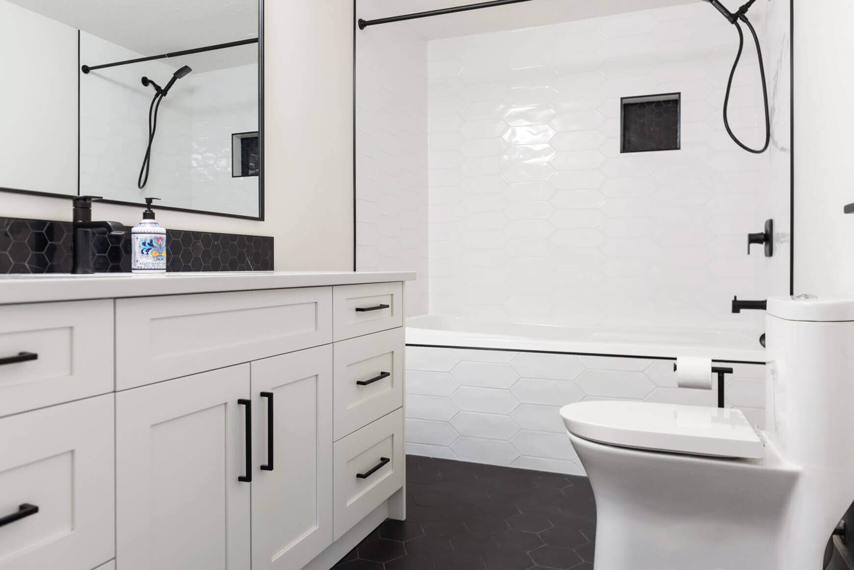 Mid-range bathroom renovation featuring white vanity with black hardware, modern toilet, and walk-in shower with white tile and glass enclosure.