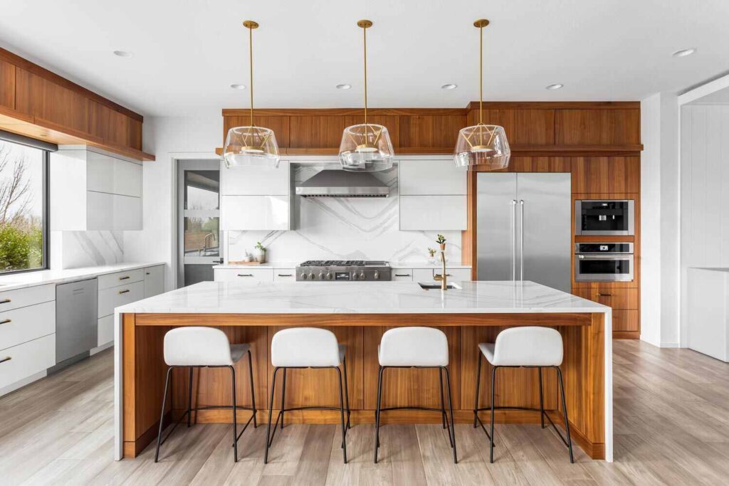 Modern kitchen featuring painted cabinet finishes with white cabinetry, warm wood accents, large island, and pendant lighting.
