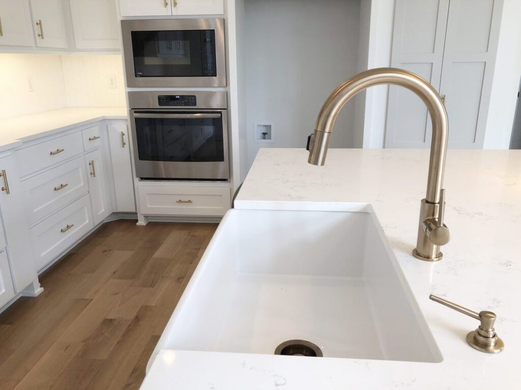 White fireclay kitchen sink with gold faucet and modern cabinetry, highlighting durable sink material and elegant kitchen design.