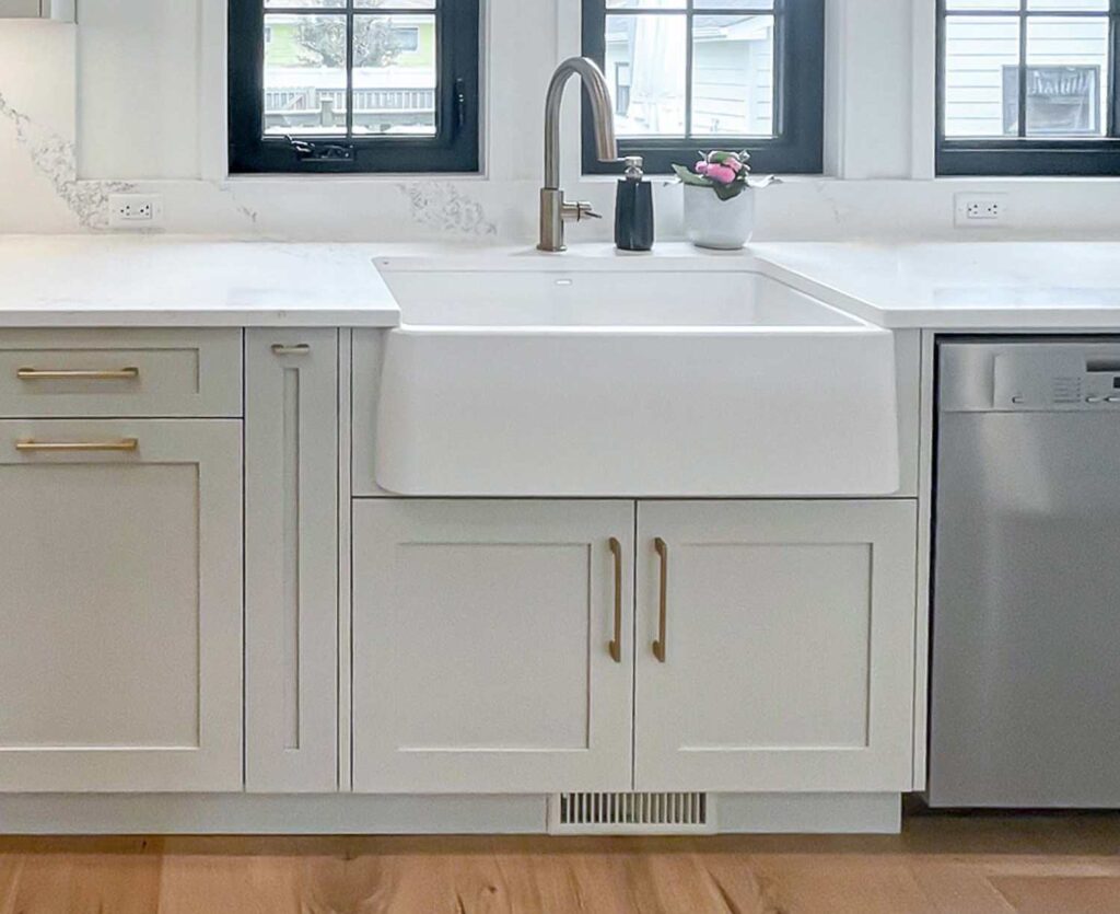 White farmhouse sink paired with light cabinetry and brass hardware, showcasing coordinated cabinet finishes in a modern kitchen.